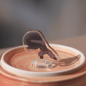 Puede incluir: Una figurita de acr&iacute;lico transparente de una persona que lleva un objeto grande en la espalda. La figurita est&aacute; de pie sobre una base circular marr&oacute;n y blanca.