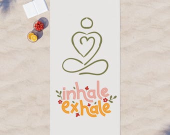 May include: White beach towel with a green line drawing of a person meditating with a heart in their chest. The text "inhale exhale" is written in pink and orange with small red flowers.