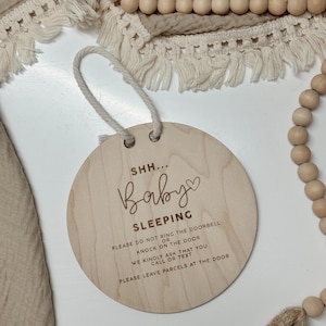 May include: A round wooden sign with the text "SHH... Baby Sleeping" and instructions to not ring the doorbell or knock on the door, but to call or text instead. The sign also says to leave parcels at the door.