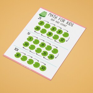 以下が含まれることがあります： 子供たちがスキップカウントの練習をするための印刷可能なワークシートです。ワークシートには、カエルのイラストと、数字が書かれたスイレンの葉がいくつか描かれています。数字は、子供たちが2、5、10ずつスキップカウントすることを学ぶのに役立つパターンで配置されています。