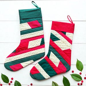 Può includere: Due calze di Natale fatte a mano con un design patchwork. Le calze presentano tessuti rossi, bianchi e verdi con motivi floreali e a pois. Ogni calza ha un anello verde per appenderla.