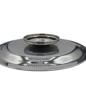 Op de afbeelding: Een cirkelvormig, gepolijst zilverkleurig metalen deksel met een glad, reflecterend oppervlak en een centrale, verhoogde ronde handgreepknop. Het deksel heeft een licht gewelfd profiel met een strakke, metalen afwerking die het licht weerkaatst.