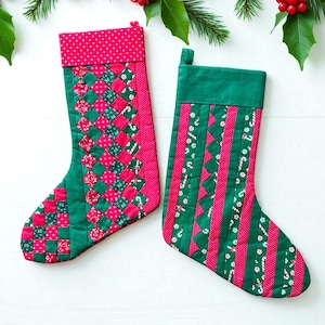 Può includere: Due calze di Natale con disegni patchwork verdi e rossi. Una calza ha un motivo intrecciato, l'altra ha strisce verticali con accenti di bastoncini di zucchero. Entrambe hanno polsini a pois rossi e sono decorate con agrifoglio.