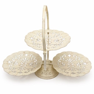 May include: Off-white, three-tiered serving stand with a handle. The plates have a scalloped edge and a floral cut-out design. The stand is made of metal and has a distressed finish, perfect for displaying desserts or appetizers.