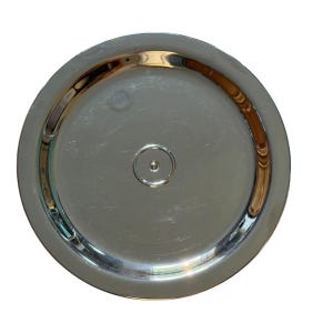 Op de afbeelding: Een cirkelvormig, gepolijst zilverkleurig metalen bord of dienblad met een glad, reflecterend oppervlak. Het object is voorzien van een verhoogde buitenrand en een kleine, gecentreerde cirkelvormige inkeping voor een strakke uitstraling.