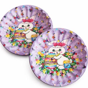 May include: Two purple, scalloped-edge plates with a painted Easter theme. Each plate features a white bunny with a pink bow, painting a colorful Easter egg, surrounded by flowers.