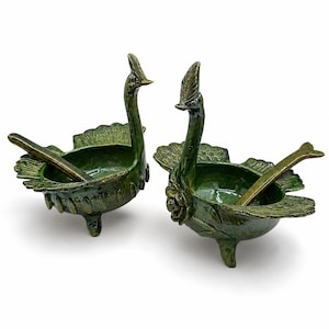 May include: Two matching dark green glazed ceramic bowls shaped like birds with long necks and crests. Each bowl features a sculpted tail, three small feet, and a matching spoon resting inside. The exterior is decorated with embossed floral details.