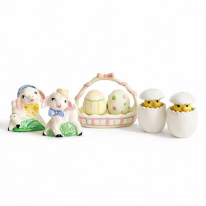 May include: A collection of Easter-themed ceramic figurines. Includes two lamb figurines, a basket with two egg-shaped salt and pepper shakers, and two chick-in-egg salt and pepper shakers. The figurines are white, with pastel accents.