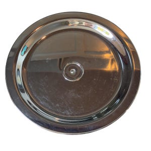 Op de afbeelding: Een cirkelvormig luchtfilterdeksel van gepolijst chroommetaal met een glad, reflecterend oppervlak en een verhoogd centraal bevestigingspunt. De metalen afwerking vertoont subtiele lichtreflecties en kleine krasjes op de ronde plaat.