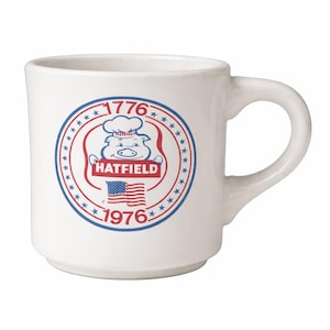 May include: White ceramic mug with a curved handle. The mug features a circular design with a pig wearing a chef's hat, the word "HATFIELD" in a red banner, and the American flag. The design is framed by the years 1776 and 1976.