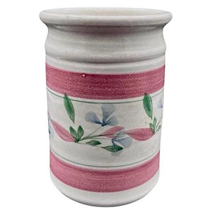 May include: A ceramic utensil holder with a white base, adorned with a pink band and floral patterns. The cylindrical holder features a slightly flared rim and is decorated with blue and green floral accents.
