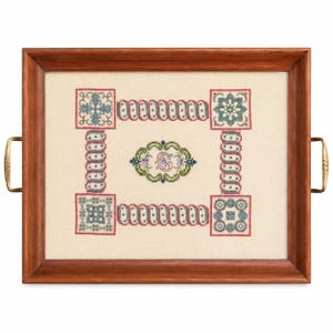 May include: A rectangular wooden serving tray with gold-toned metal handles. The center features a cream-colored fabric panel decorated with a cross-stitch pattern in red, green, blue, and pink, including a central floral motif with the letter S.
