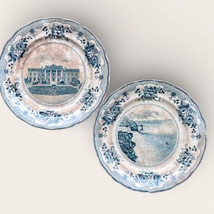 Op de afbeelding: Twee decoratieve borden met een blauw-witte bloemenrand. Eén bord toont het Witte Huis, de andere een waterval. De borden hebben een geschulpte rand en een vintage esthetiek.