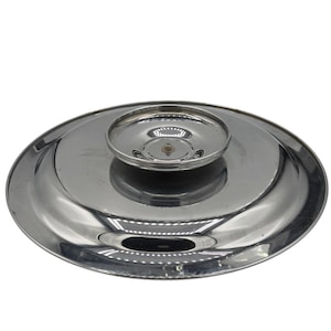 Op de afbeelding: Een cirkelvormig, gepolijst zilverkleurig metalen deksel met een glad, reflecterend oppervlak en een verhoogde, komvormige handgreep in het midden. Het deksel heeft een brede, platte rand die naar de centrale knop toe taps toeloopt.