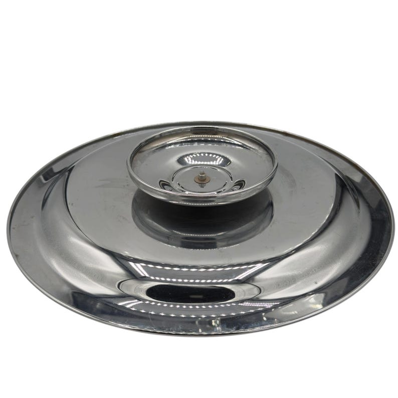 Op de afbeelding: Een cirkelvormig, gepolijst zilverkleurig metalen deksel met een glad, reflecterend oppervlak en een verhoogde, komvormige handgreep in het midden. Het deksel heeft een brede, platte rand die naar de centrale knop toe taps toeloopt.