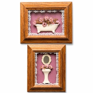 May include: Two rectangular wooden frames containing shadow box art. The top frame features a white ceramic bathtub filled with pink flowers on a purple polka dot background with white lace trim. The bottom frame shows a white pedestal sink.