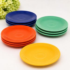 May include: A collection of colorful ceramic plates in shades of blue, green, orange, and yellow. Each plate has a circular design in the center and a slightly raised rim. The plates are stacked in neat piles, showcasing a vibrant and cheerful aesthetic.