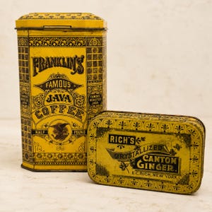 May include: A tall, rectangular yellow metal tin labeled Franklin's Famous Java Coffee and a smaller, horizontal rectangular yellow metal tin labeled Rich's Crystallized Canton Ginger, both featuring black decorative patterns and typography.