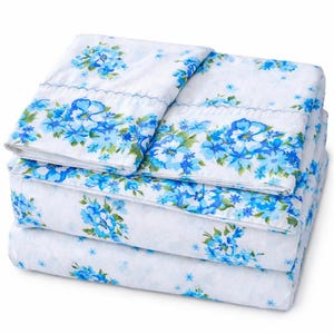 May include: A stack of white bed sheets with a blue floral pattern. The sheets feature a repeating pattern of blue flowers and green leaves. The top sheet has a decorative border with a scalloped edge.