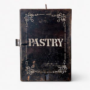 Könnte beinhalten: Eine Vintage-Backwarenbox aus schwarzem Metall mit weißen Buchstaben und dekorativen Eckdesigns. Das Wort "PASTRY" ist prominent auf der Vorderseite zu sehen. Die Box hat einen Schnappverschluss und einen kleinen Griff oben.