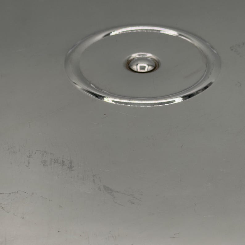 Op de afbeelding: Een gepolijst zilverkleurig metalen oppervlak met een cirkelvormige inkeping in het midden bovenaan. Het gladde, reflecterende materiaal vertoont subtiele krassen en lichte schaafplekken over het onderste deel van de metalen plaat.