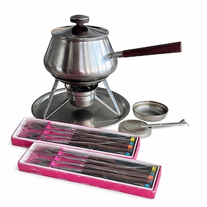 Puede incluir: Un juego de fondue de acero inoxidable con mango y pomo de tapa de madera oscura. Incluye un soporte para calentar, quemador, cuencos pequeños y dos cajas de tenedores de fondue con puntas de colores. Un juego completo.