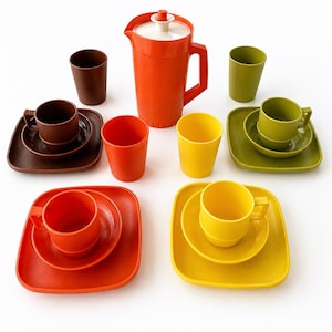 Puede incluir: Un conjunto de vajilla retro colorida, que incluye tazas, platillos y una jarra. El juego presenta tonos de naranja, marrón, amarillo y verde. Las tazas y platillos son cuadrados, y la jarra tiene una tapa blanca.