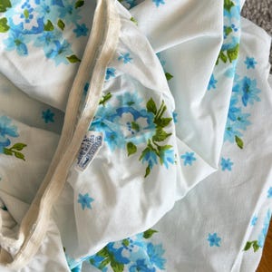 May include: White fitted sheet with a blue floral pattern and green leaves. The sheet has an elastic band and a tag that reads "Hurley Mattress Grand Tone". The floral design is repeated across the fabric.