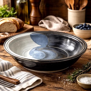 May include: A large, handcrafted ceramic bowl with a black exterior and a white and blue interior design. The bowl has a wide rim and a glossy finish, perfect for serving salads or pasta dishes. The bowl is approximately 12 inches in diameter.