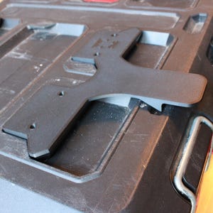 May include: Close-up of a black plastic toolbox with a grey metal handle and red accents. A black, T-shaped piece is attached to the top. The toolbox has several compartments and is designed for tool storage.