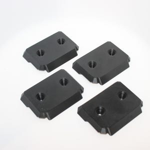 May include: Four black rectangular metal components with beveled edges and two circular holes each, arranged on a white surface. These appear to be parts or fittings.