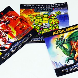 Może przedstawiać: Trzy kasety do gry Sega Mega Drive. Pierwsza kaseta jest czerwono-pomarańczowa z tekstem "FATAL FURY 2" i "MEGA DRIVE". Druga kaseta jest niebiesko-zielona z tekstem "TEENAGE MUTANT HERO TURTLES&reg; THE HYPERSTONE HEIST&trade; KONAMI". Trzecia kaseta jest niebiesko-zielona z tekstem "ALUSIA DRAGOON" i "MEGA DRIVE".