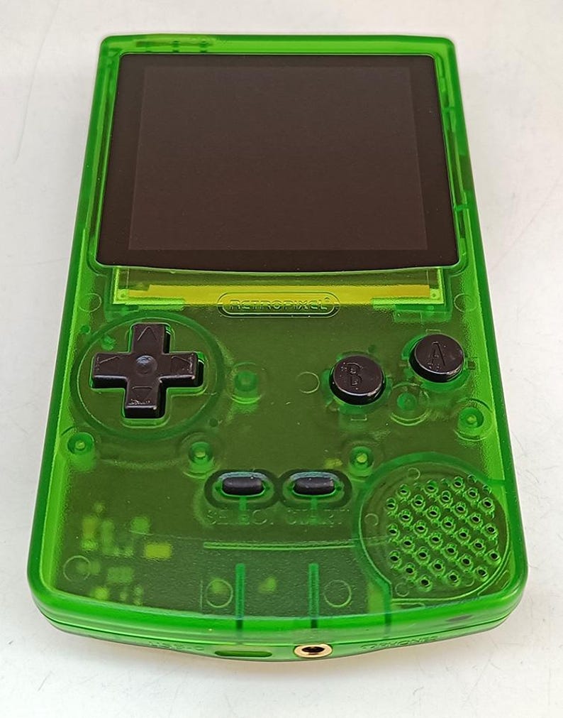 Puede incluir: Una consola de juegos port&aacute;til verde transparente con pantalla negra, cruceta y botones. El texto "RETROPIXEL" es visible. La consola tiene un altavoz y una toma de auriculares.