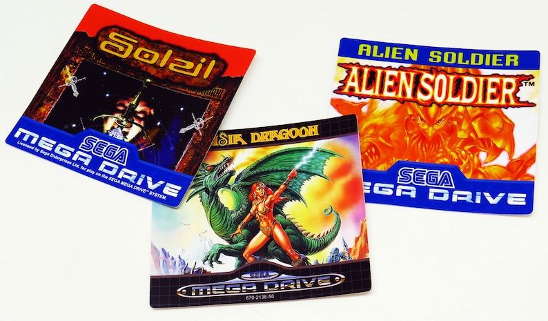 Może przedstawiać: Trzy kasety do gry Sega Mega Drive z kolorowymi etykietami. Etykiety przedstawiają tytuły gier "Alien Soldier", "Sir Dragoon" i "Sol-Dail".