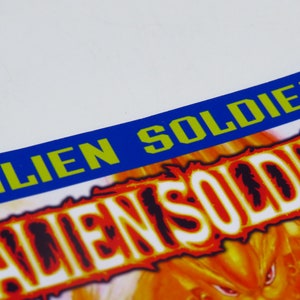 Może przedstawiać: Niebiesko-zielony baner z napisem "ALIEN SOLDIER" białymi literami. Baner znajduje się nad ognistym pomarańczowo-ż&oacute;łtym tłem z napisem "ALIEN SOLDIER" białymi literami.
