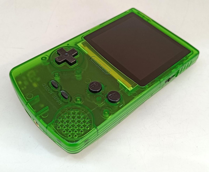 Puede incluir: Consola de juegos port&aacute;til verde transparente con pantalla negra y botones negros. La consola cuenta con una cruceta, botones select y start, y botones A y B. El logotipo de Nintendo es visible.