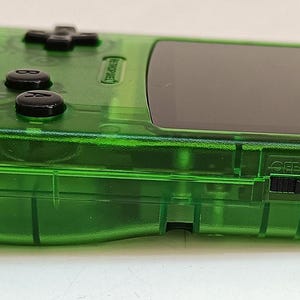 Puede incluir: Una consola de juegos port&aacute;til verde transparente. El dispositivo presenta una pantalla negra, botones de control negros y un altavoz. El dise&ntilde;o de la consola incluye una cruceta, botones de acci&oacute;n y un interruptor de encendido. La carcasa de pl&aacute;stico es de un verde vibrante y transparente.