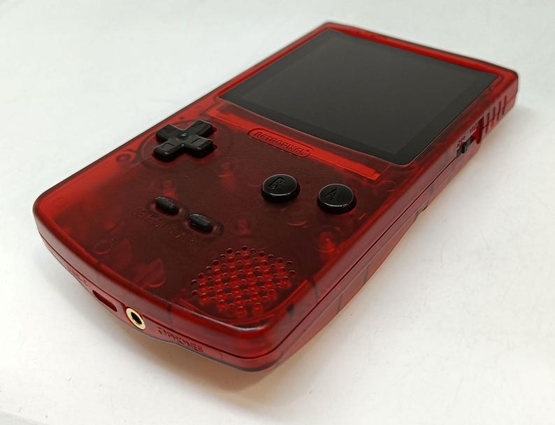 May include: A transparent red handheld gaming console with a black screen, directional pad, and buttons. The console has a speaker, headphone jack, and a power switch. The Nintendo logo is visible.
