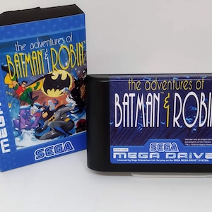 May include: A Sega Mega Drive game cartridge for the game "The Adventures of Batman & Robin". The cartridge is black with a blue label featuring the game title and Sega logo. The game features Batman and Robin in a snowy scene with the Joker and Mr. Freeze.