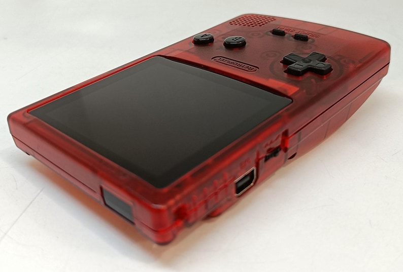 May include: A transparent red handheld gaming console with a black screen and black buttons. The console has a directional pad and two action buttons. The word "Nintendo" is visible on the device.