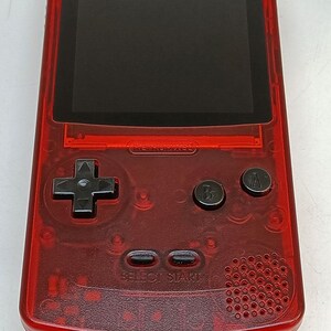 May include: A transparent red handheld gaming console with a black screen and black buttons. The console has a directional pad, two action buttons, and select/start buttons. The text "RETROPIXEL" is visible on the device.