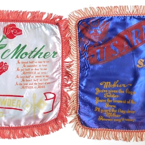 May include: Two square satin souvenir pillows with fringed edges. The left pillow is white with red roses, the text "Mother" and "Camp Crowder MO". The right pillow is blue with "U.S. Army Fort Sheridan Illinois" text, a tower illustration, and gold lettering.