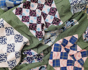 Puede incluir: Una colcha de patchwork con un patrón repetitivo de cuadrados en varias telas, incluyendo verde oscuro con puntos blancos, cuadros azul marino y rosa claro con estampados florales o geométricos oscuros, todo unido con costuras visibles.
