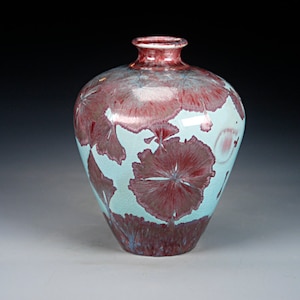 May include: A small, round ceramic vase with a white glaze and a red and pink floral pattern.