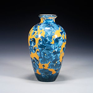 May include: A ceramic vase with a narrow neck and a rounded body, featuring a vibrant mustard yellow base glaze overlaid with deep blue crystalline patterns that resemble blooming flowers or starbursts, with a dark blue base and rim.