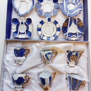 Peut inclure: Un ensemble de 10 tasses à thé miniatures et soucoupes dans une boîte blanche. Les tasses et les soucoupes sont décorées de motifs floraux bleus et dorés.