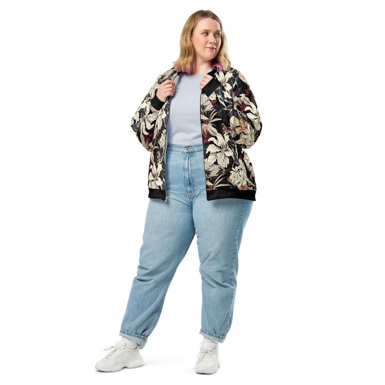 May include: A black bomber jacket with a floral print featuring white, beige, and red flowers. The jacket has a zipper closure and a ribbed collar, cuffs, and hem. The model is wearing blue jeans and white sneakers.