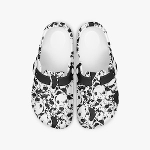 May include: Pair of white clogs with a black and white Dalmatian dog pattern. The clogs have a black strap and a white interior. The Dalmatian pattern features various dog faces and spots.