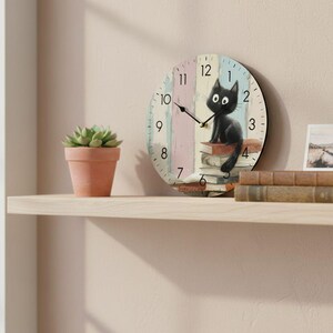 Peut inclure: Une horloge murale ronde avec une illustration de chat noir. Le cadran de l'horloge présente un fond à rayures pastel avec des chiffres et des aiguilles noirs. Le chat est assis sur une pile de livres. Une petite plante succulente en pot est sur une étagère.