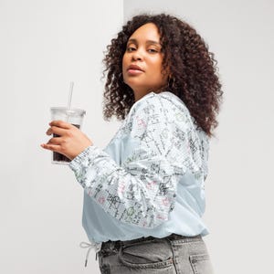 May include: A light blue windbreaker jacket with a white grid pattern and colorful mathematical equations printed on the sleeves and back. The jacket has a drawstring waist and is paired with gray jeans.